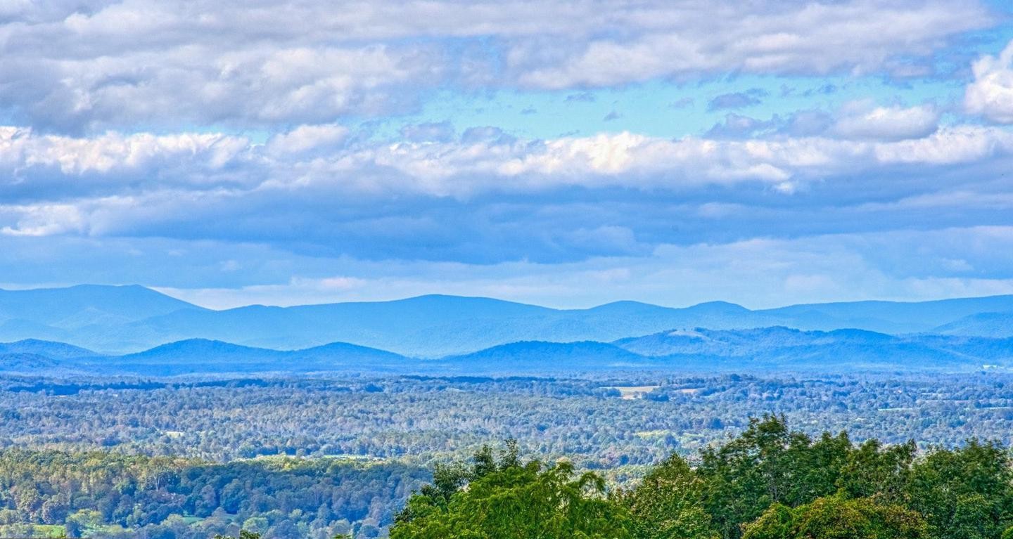 Layered Blue Ridge mountain ridges beyond wooded Virginia countryside under a cloudy sky